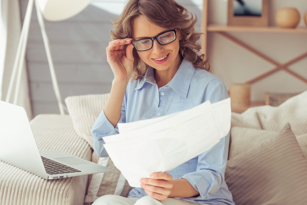Kobieta siedzi na kanapie i czyta przewodnik po ubezpieczeniu nieruchomości