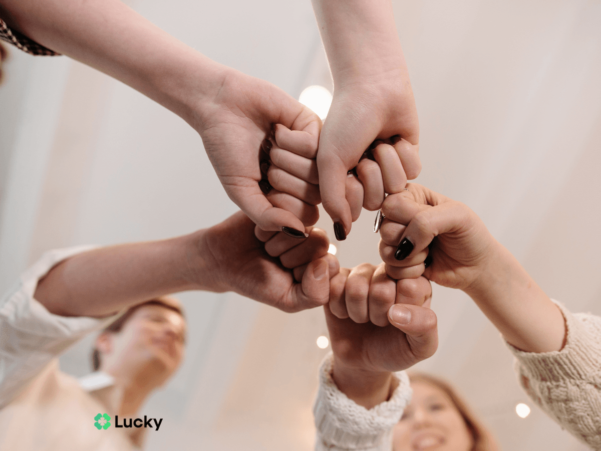 Wspólny uścisk dłoni grupy osób symbolizujący jedność, współpracę i wsparcie, ilustrujący korzyści jakie daje grupowe ubezpieczenie na życie. Na obrazku widoczne jest logo Lucky